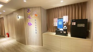 Zona de recepción de hotel con un quiosco digital, un extintor y un cartel con caracteres chinos.