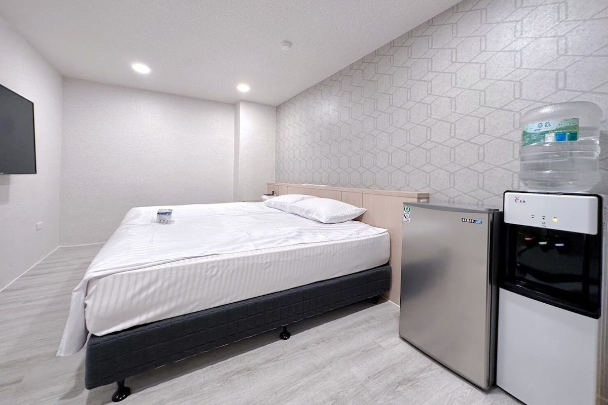 Quarto de hotel com cama, dispensador de água e um pequeno frigorífico.