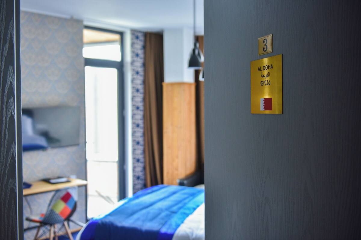 Une chambre d’hôtel avec un lit, un bureau et une chaise. Un panneau sur le mur indique le numéro de la chambre : 3.