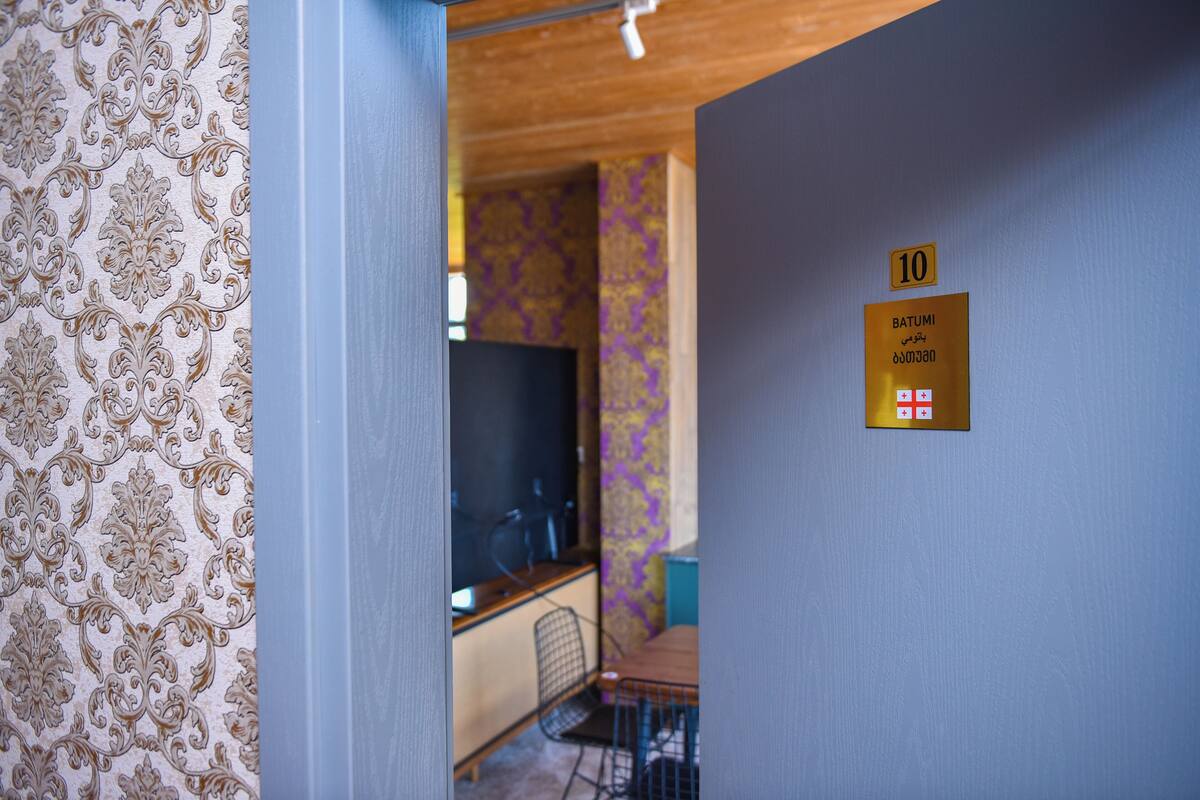 Une pièce dont les murs sont recouverts d’un papier peint à motifs, un panneau indiquant le numéro de la pièce (10), et une porte qui donne sur une autre pièce.