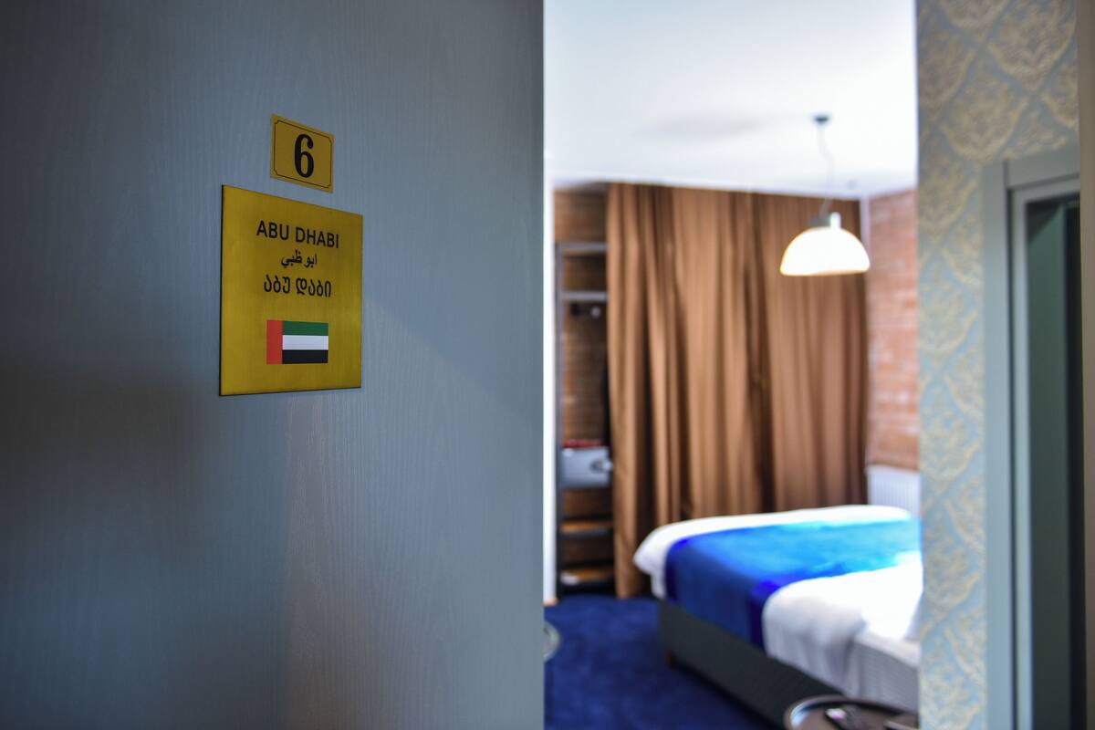 Une chambre d’hôtel avec un lit, un luminaire suspendu et une porte sur laquelle est affiché un panneau indiquant le numéro de chambre : 6.