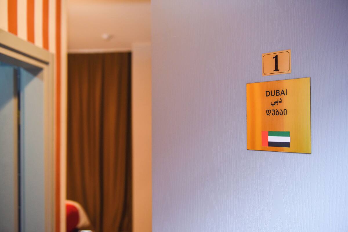 Un mur sur lequel est affiché un panneau indiquant le numéro de la salle (1) et le nom « DUBAÏ », ainsi que le drapeau des Émirats arabes unis.
