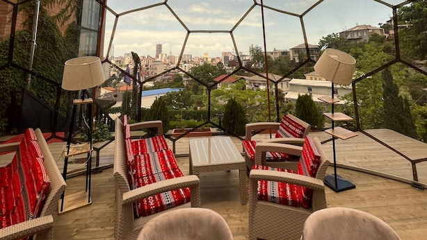 Une terrasse sur le toit dotée de panneaux de verre hexagonaux, de meubles en osier et offrant une vue sur la ville.