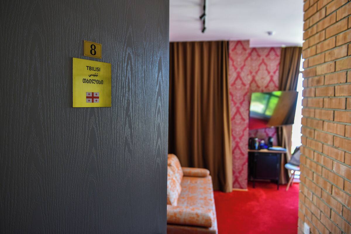 Une chambre d’hôtel avec un tapis rouge, un canapé, un téléviseur posé sur un meuble et un mur en briques.