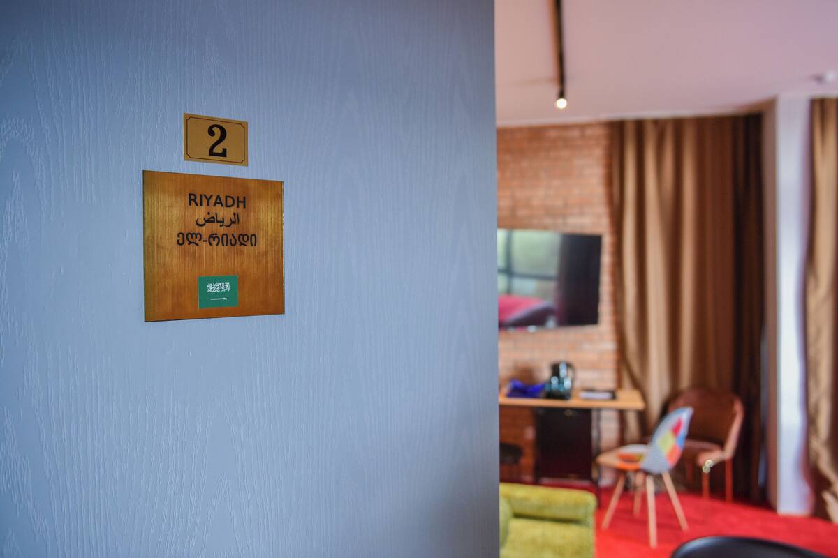 Une pièce avec une plaque en bois indiquant le numéro 2, un lit, un bureau avec une chaise et un téléviseur.