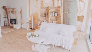 Un salón decorado en tonos blancos, con un sofá blanco, una mesita de centro redonda y una estantería.