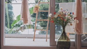 Una habitación con un ventanal grande, una escalera de madera, un florero con flores y una cesta colgante con plantas.