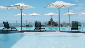 Zona de piscina con sillones de descanso y sombrillas, cielo despejado y vista al océano.