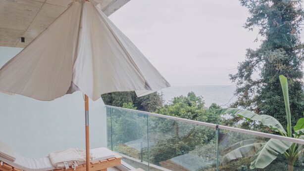 Un balcón con una cama de madera, un dosel blanco y vistas al mar y al verdor.
