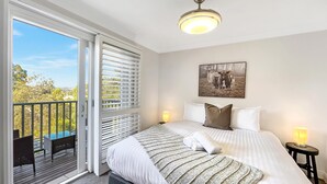Een hotelkamer met een groot bed, een plafondventilator, een schilderij van paarden en een balkon met rieten meubilair.