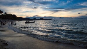Una playa con un bote, gente y montañas al fondo.
