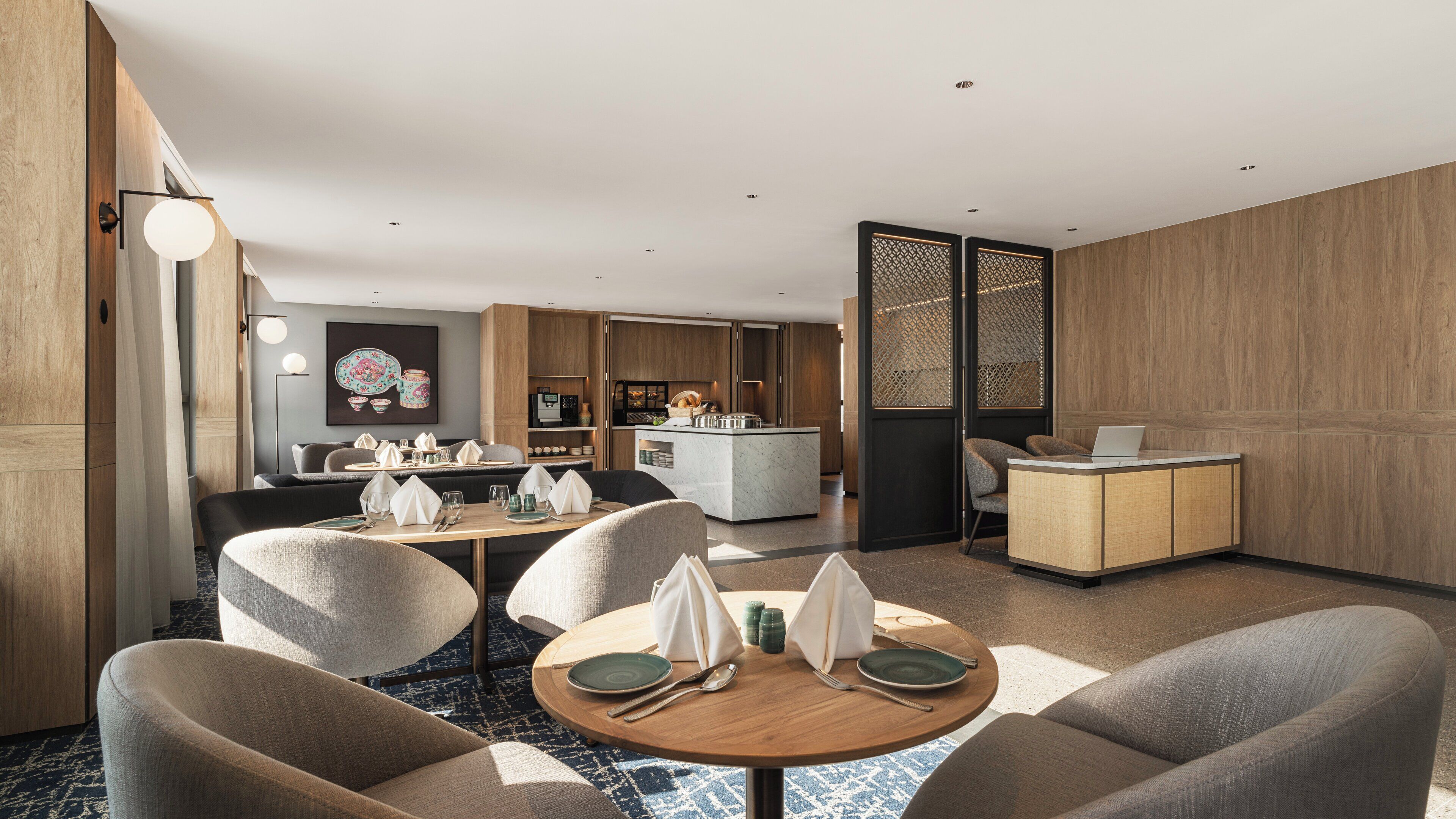 A modern hotel room with a dining area, a kitchen, and a seating area with a laptop on a desk.