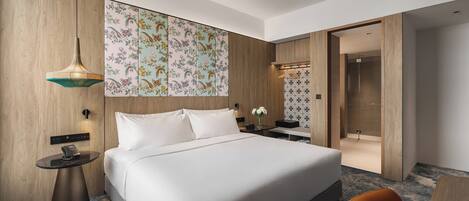 A modern hotel room with a large bed, a round side table with a phone, a hanging light fixture, and a decorative wall panel.