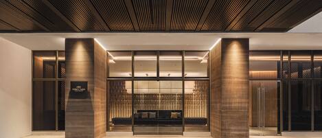 A modern hotel entrance with a reception desk, a seating area, and a wooden ceiling.