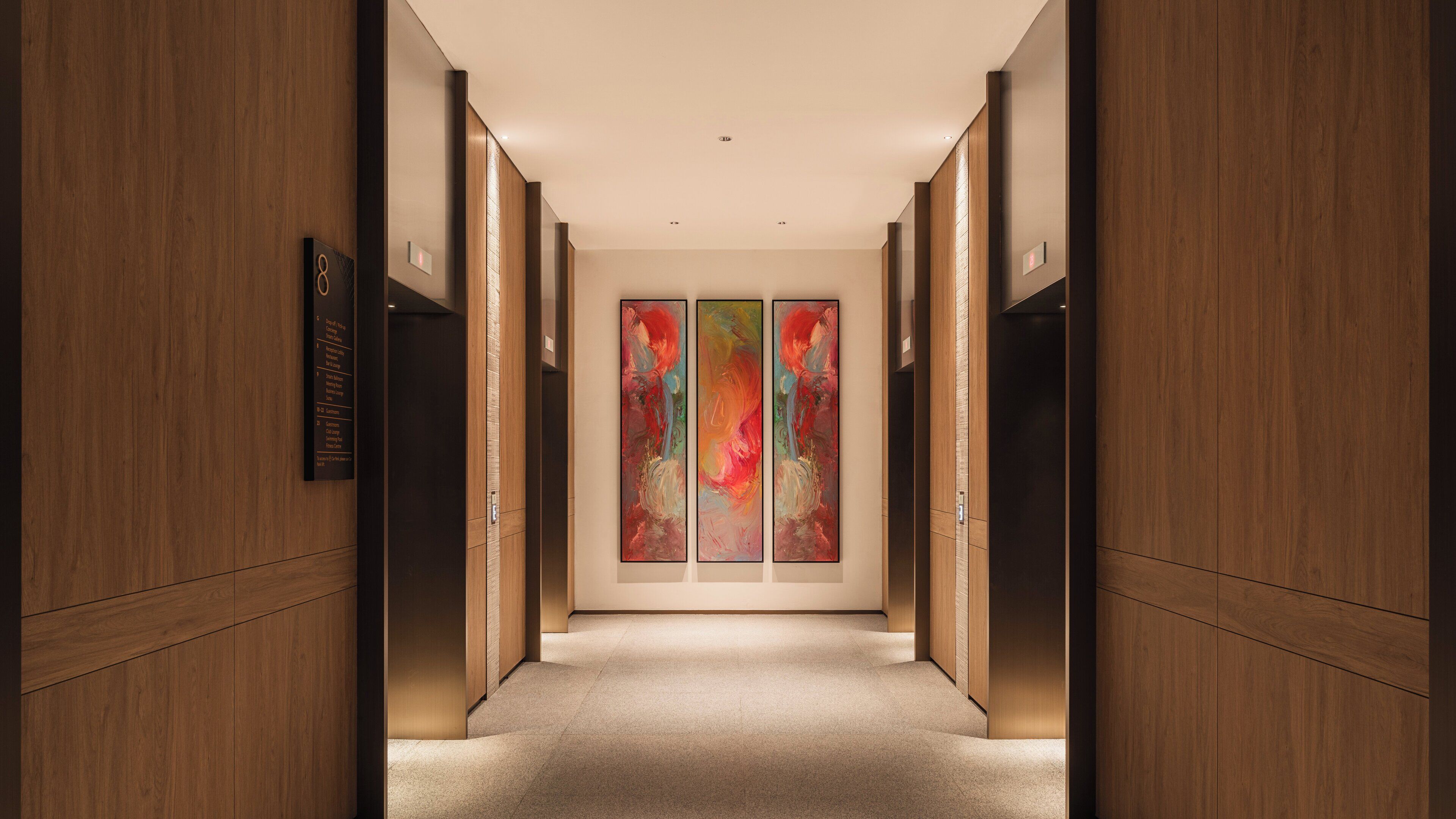 A hallway with wooden paneling, a carpeted floor, and a wall-mounted sign with room information.