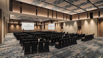 Un salón de conferencias en Crowne Plaza con filas de sillas, una pantalla grande y una alfombra estampada.