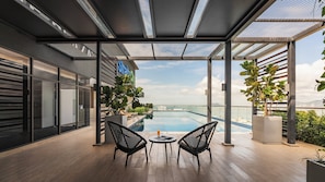 A modern outdoor pool area with two black chairs and a table, surrounded by glass walls and potted plants. - Crowne Plaza Penang Straits City by IHG (Butterworth)