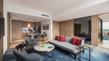 Habitación de hotel moderna con sala de estar, comedor y cocina. Hay un sofá con cojines rojos, una mesa de centro y un televisor.