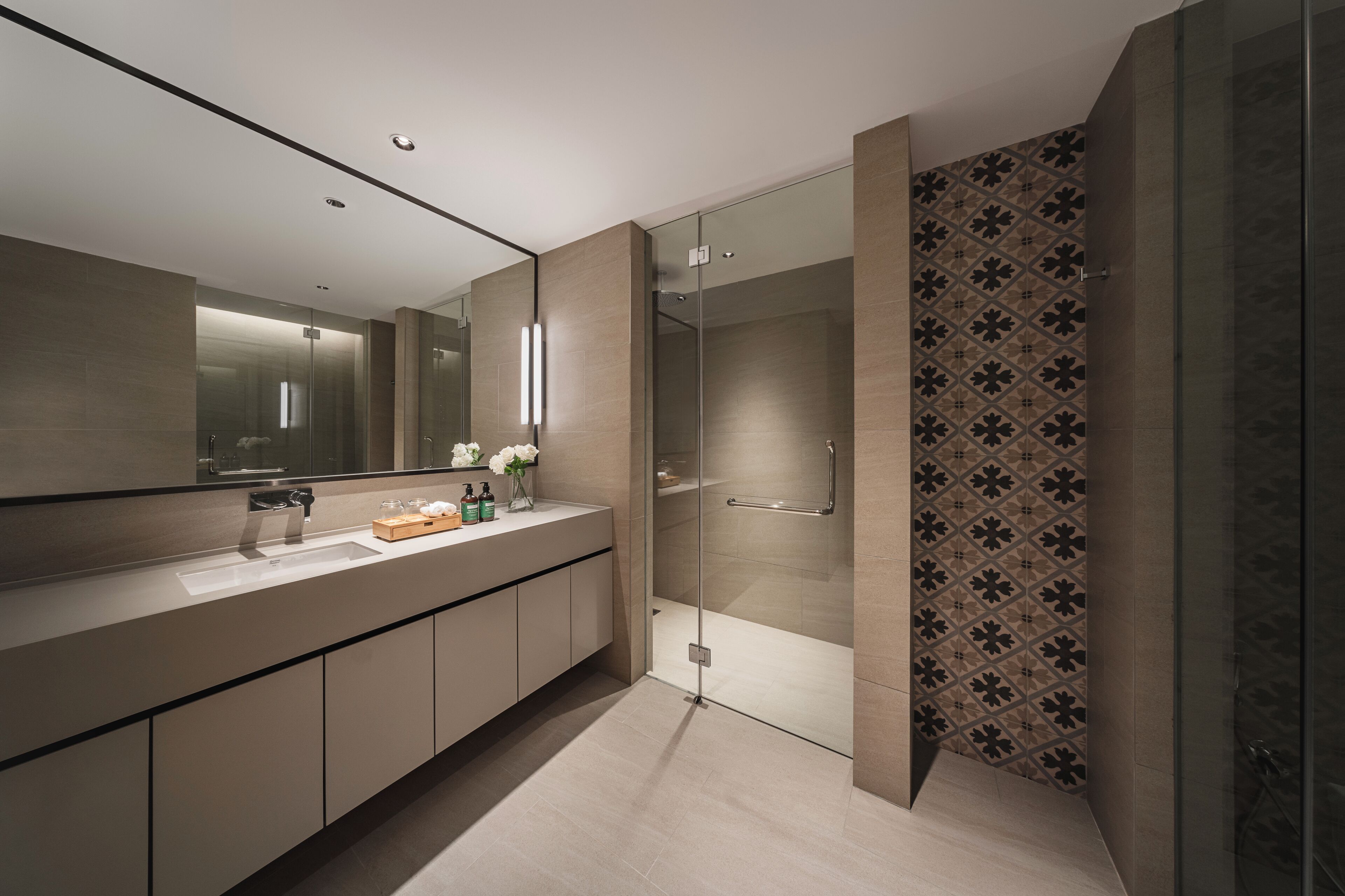 A modern bathroom with a glass shower enclosure, a large mirror, and a vanity with a sink and toiletries.