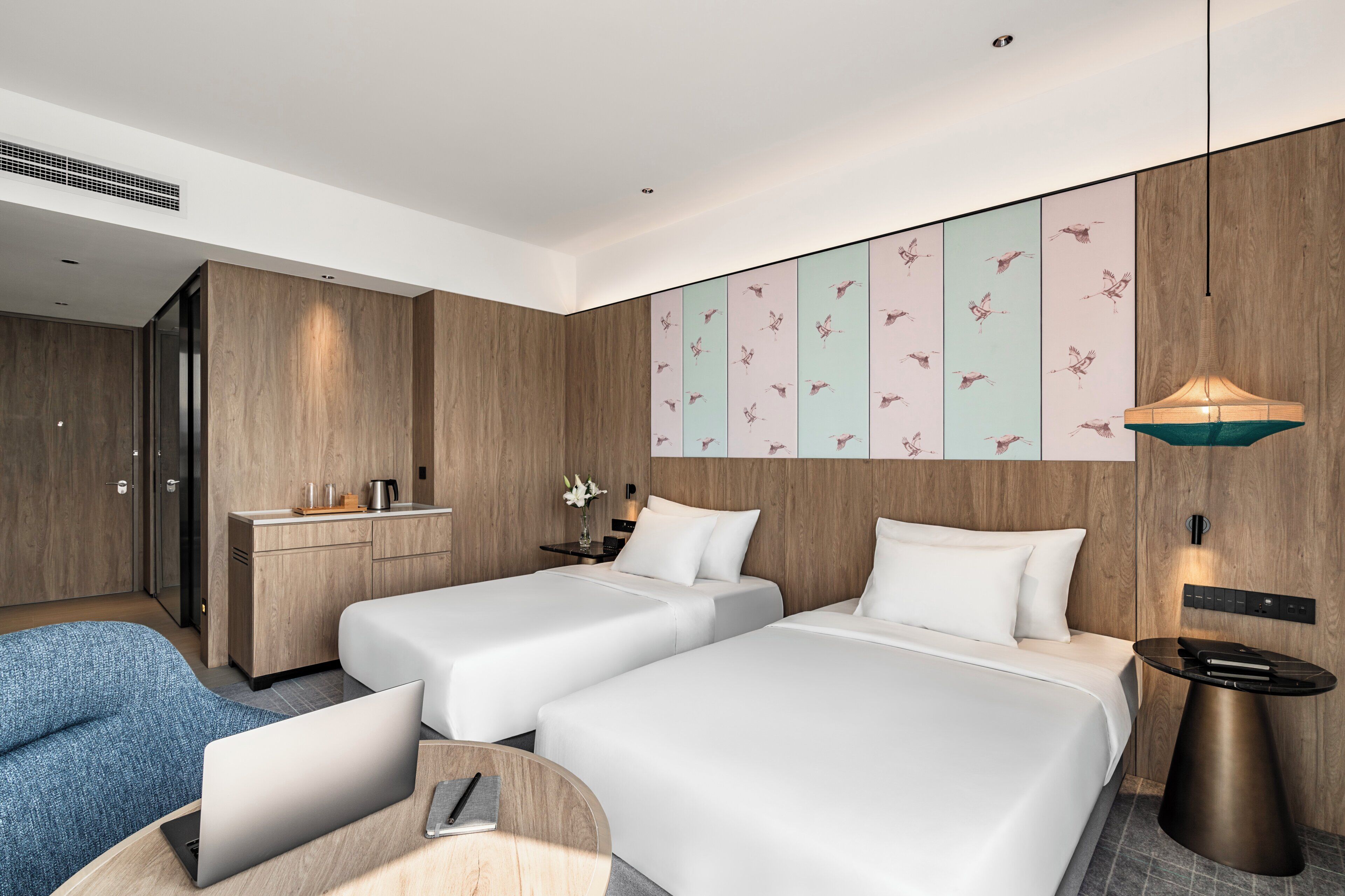 Una habitación de hotel moderna con dos camas, un escritorio, una silla y un panel decorativo en la pared.