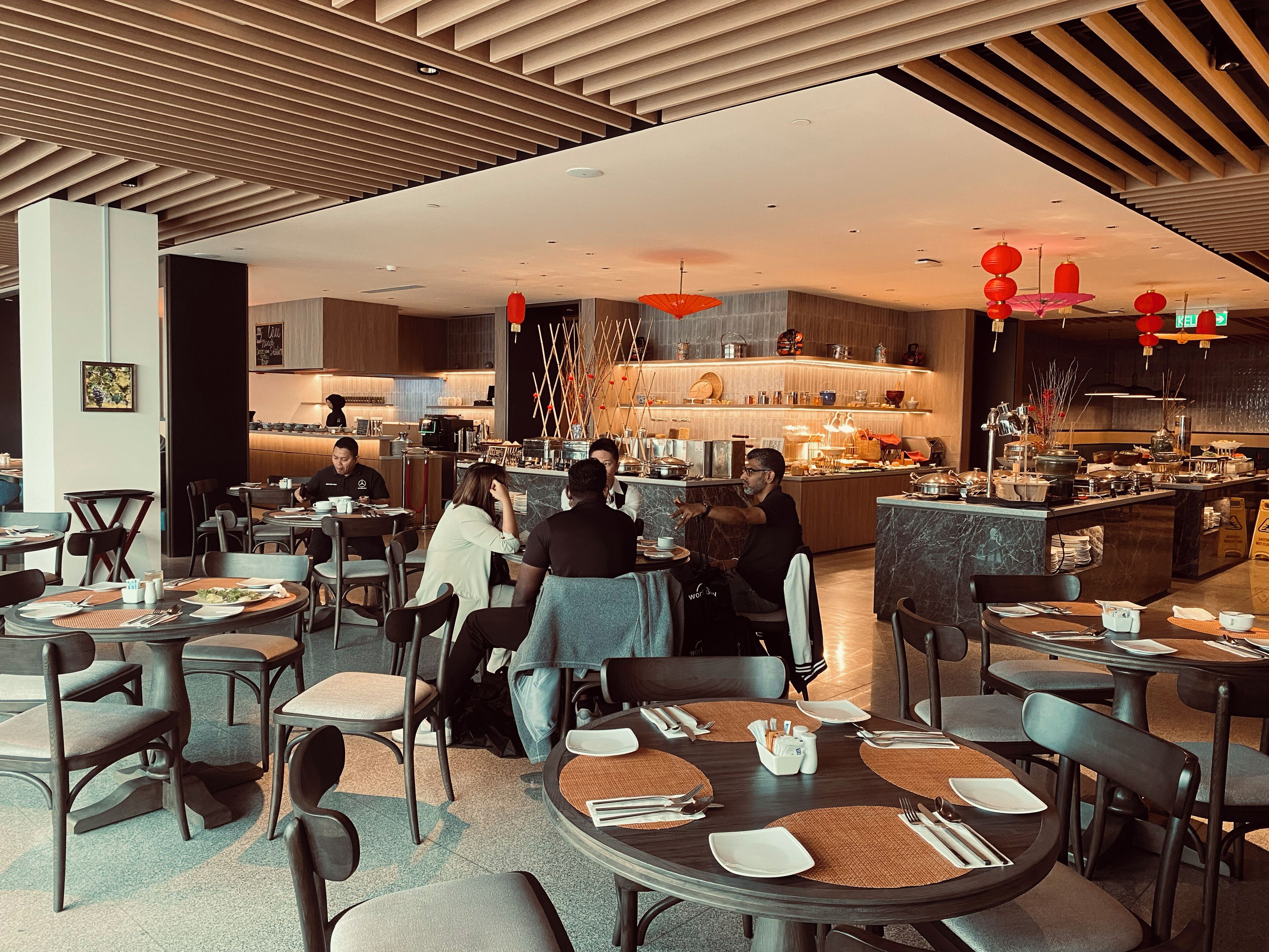 A modern restaurant with round tables, a bar area, and a kitchen in the background.