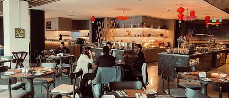A modern restaurant with round tables, a bar area, and a kitchen in the background.