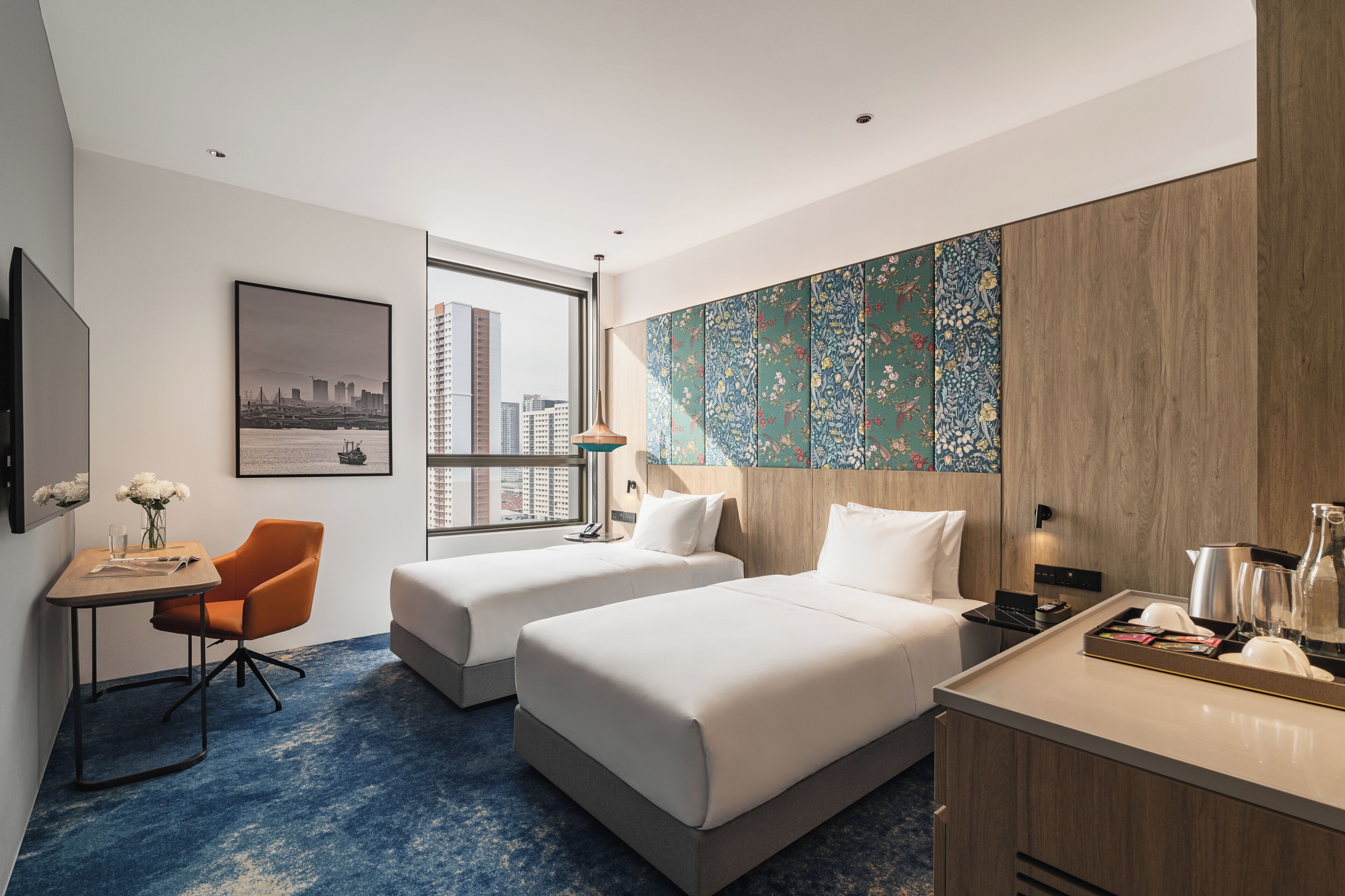 Habitación de hotel con dos camas, un escritorio con silla, vista a la ciudad y un adorno en la pared.