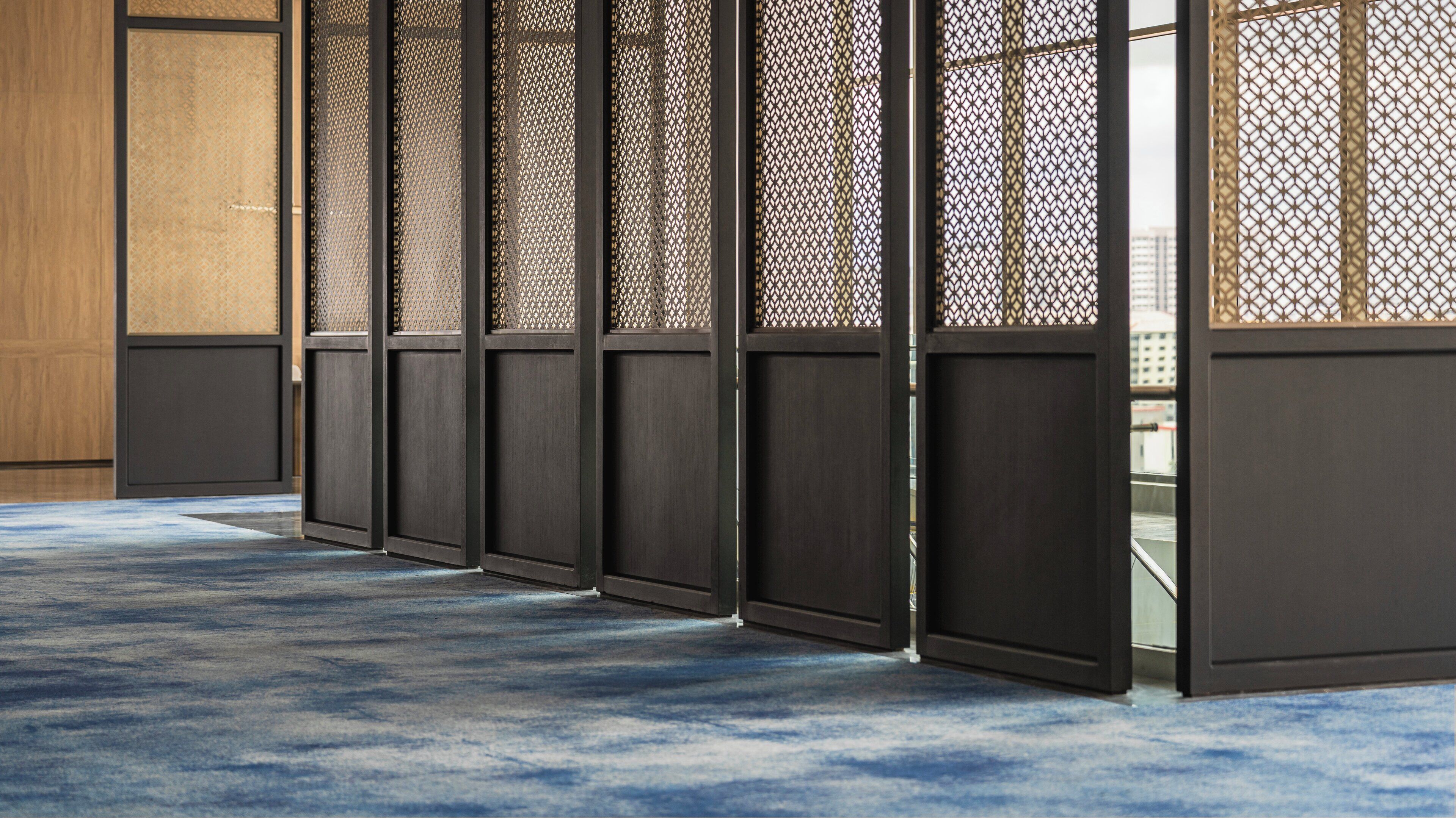 A row of traditional sliding doors with a patterned lattice design, leading to a room with a blue carpet.