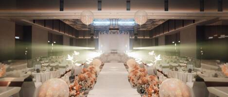 A banquet hall with a central aisle, tables on either side, and floral arrangements.