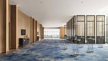 A spacious hotel lobby with a blue carpet, wooden panel walls, and a view of the city through large windows.