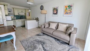 Une cuisine moderne avec des meubles blancs, une table à manger avec des chaises, un canapé beige et un tapis à motifs.