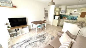 Un salon avec un canapé, une télévision, une table à manger et une cuisine en arrière-plan.