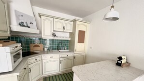 Une cuisine avec des meubles blancs, un tapis à rayures vertes, un plan de travail en marbre et un luminaire suspendu.