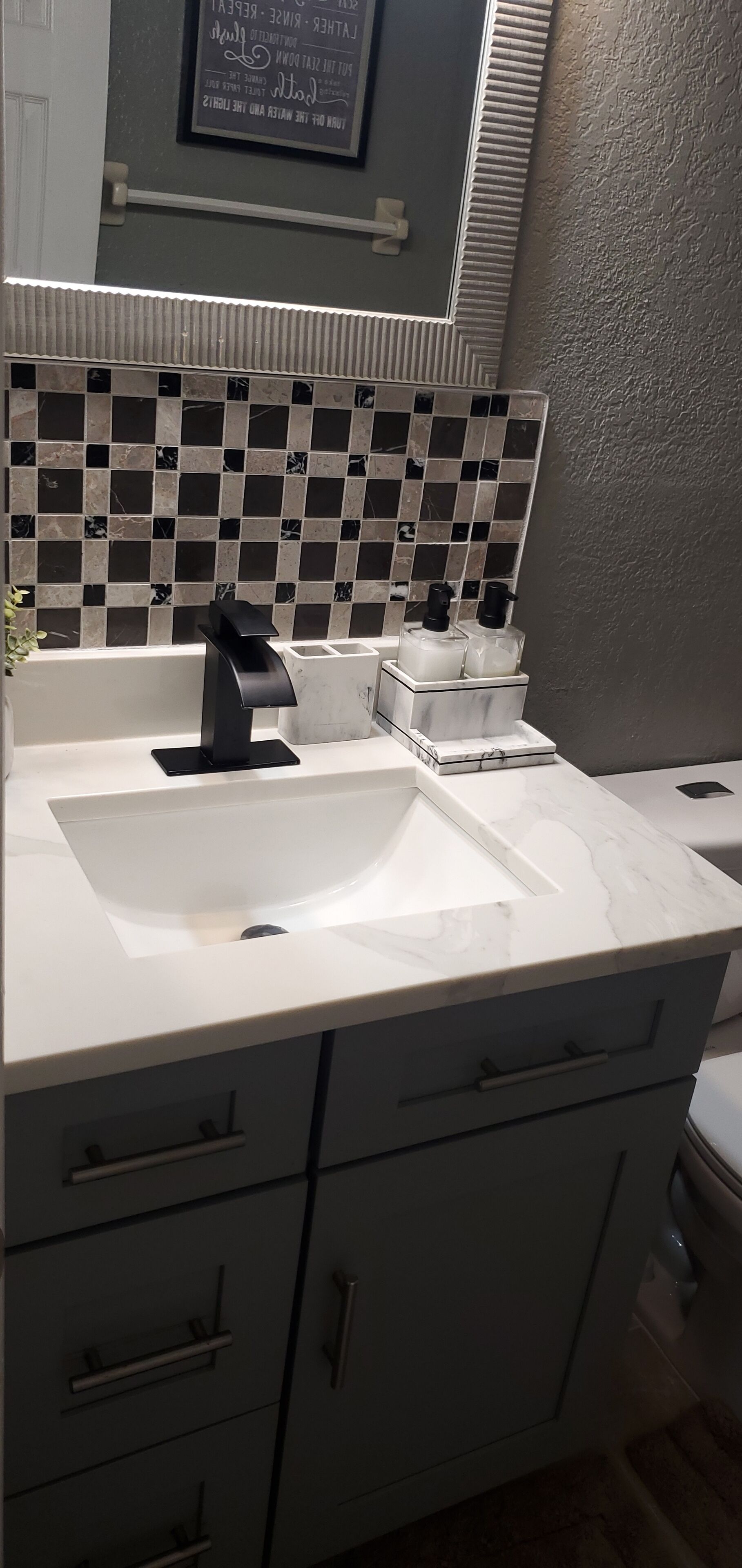 A bathroom with a white sink, black faucet, and a tiled backsplash. There are two drawers below the sink and a mirror above it.