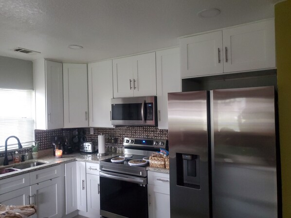 A modern kitchen with white cabinets, stainless steel appliances, a microwave, oven, and a refrigerator.