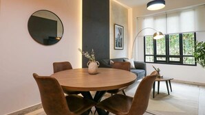 A modern dining area with a round wooden table, brown upholstered chairs, a round mirror, and a vase with flowers. - w* | Fancy 2BR in Barranco (Barranco)