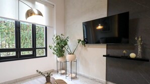 A modern living room with a large TV mounted on a dark wall, a round wooden coffee table, and two potted plants on metal stands. - w* | Fancy 2BR in Barranco (Barranco)