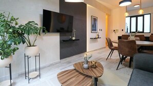 A modern living room with a flat-screen TV, a dining area with brown chairs, and a large window. - w* | Fancy 2BR in Barranco (Barranco)