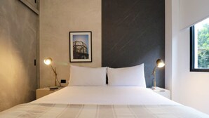 A large bed with a white and gray checkered bedspread, two bedside lamps, a framed picture on the wall, and a window on the right side. - w* | Fancy 2BR in Barranco (Barranco)