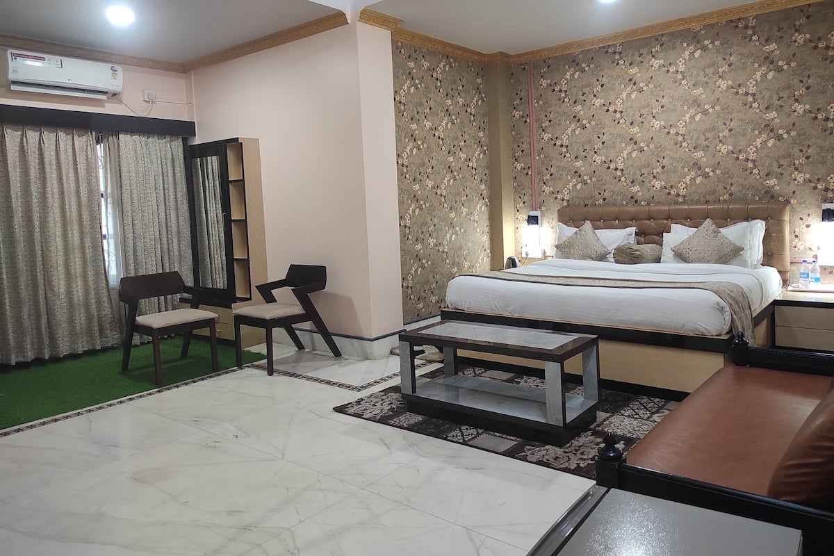 A hotel room with a bed, two chairs, a small table, and a green carpet.