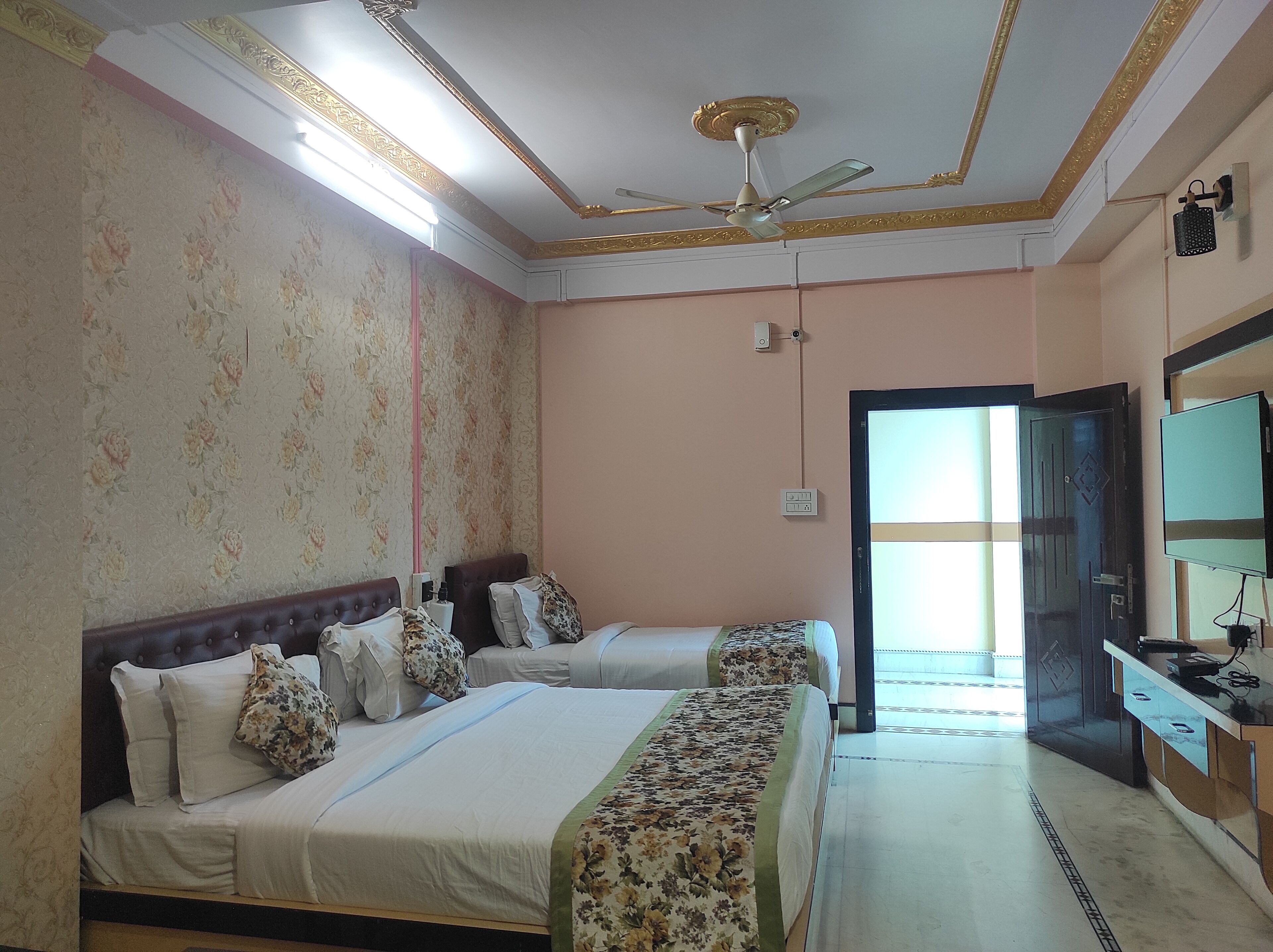 A hotel room with two beds, a ceiling fan, a TV, and a door leading to a balcony.