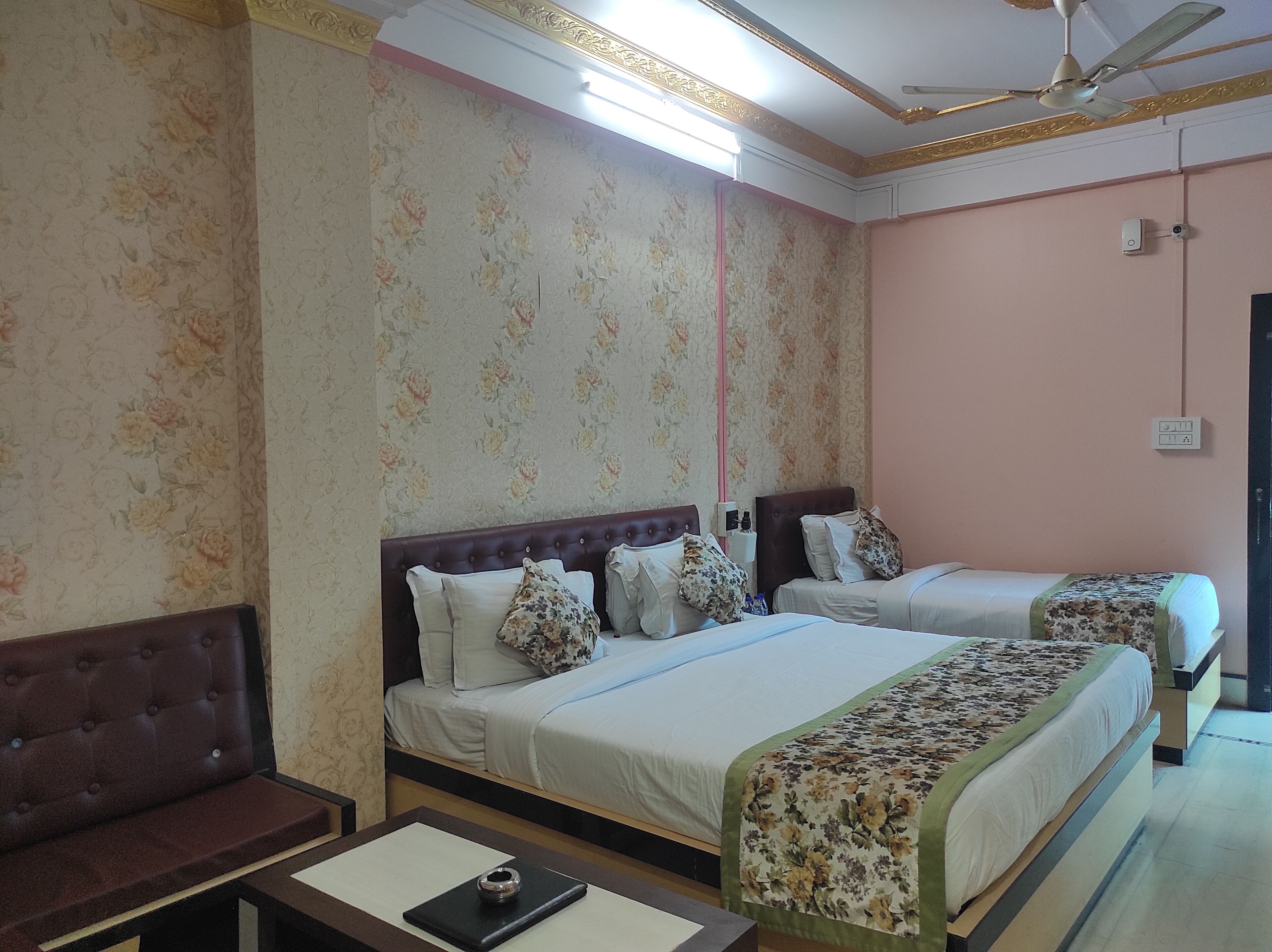 A hotel room with two beds, a sofa, a desk, and a ceiling fan.