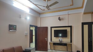 A living room with a brown leather sofa, a coffee table, a TV on a wooden cabinet, a ceiling fan, and a door.