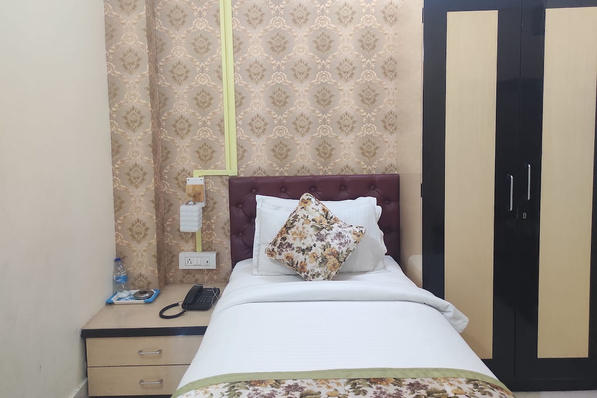 A neatly made bed with a floral pillow, a bedside phone, and a nightstand with a bottle and a tissue box.
