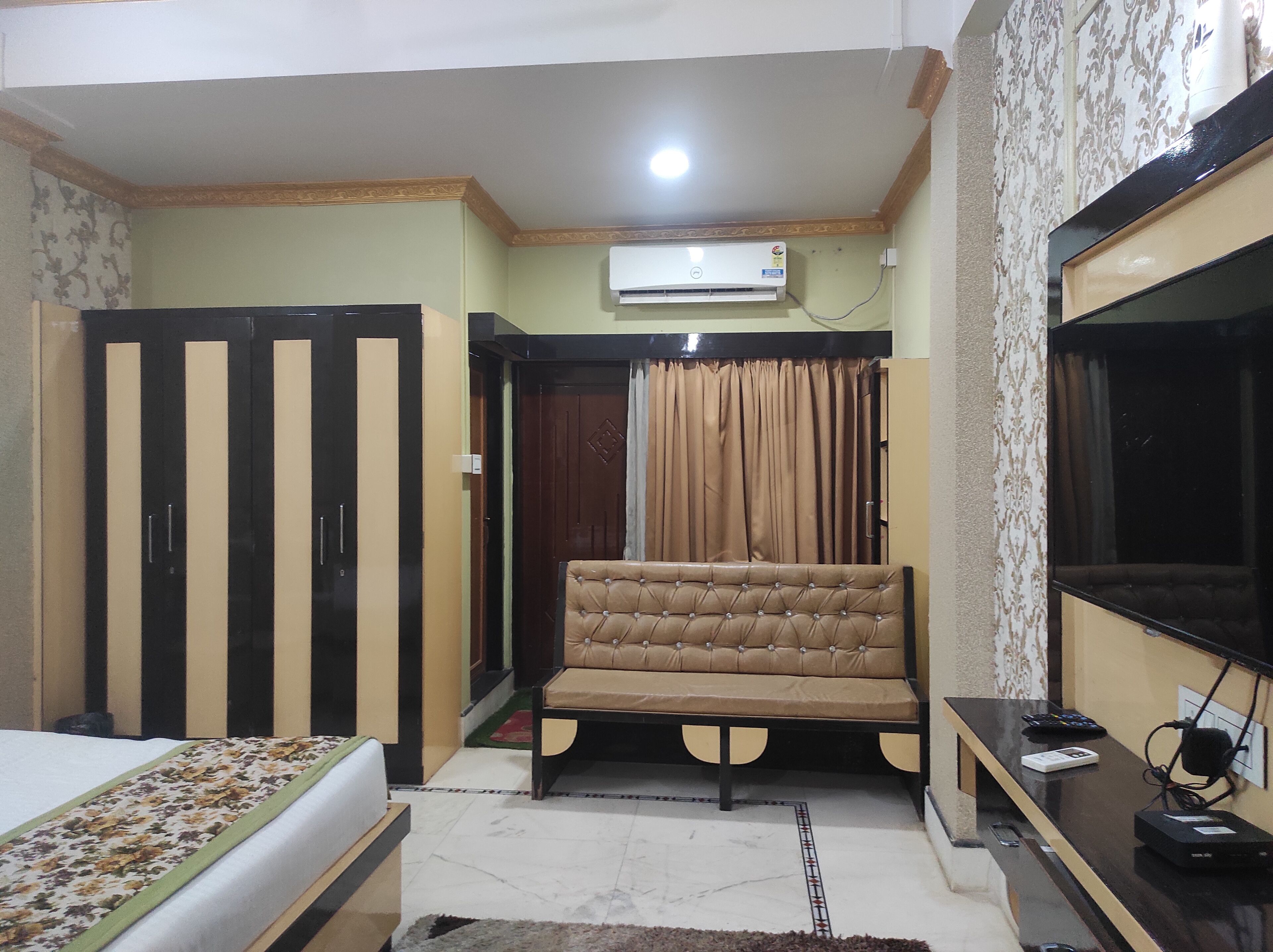 A bedroom with a bed, a sofa, a TV, and an air conditioner.