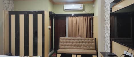 A bedroom with a bed, a sofa, a TV, and an air conditioner.