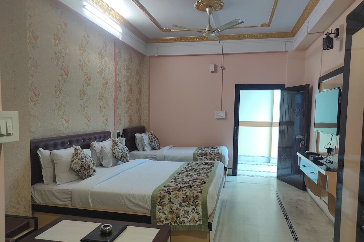 A hotel room with two beds, a desk, a TV, and a ceiling fan.