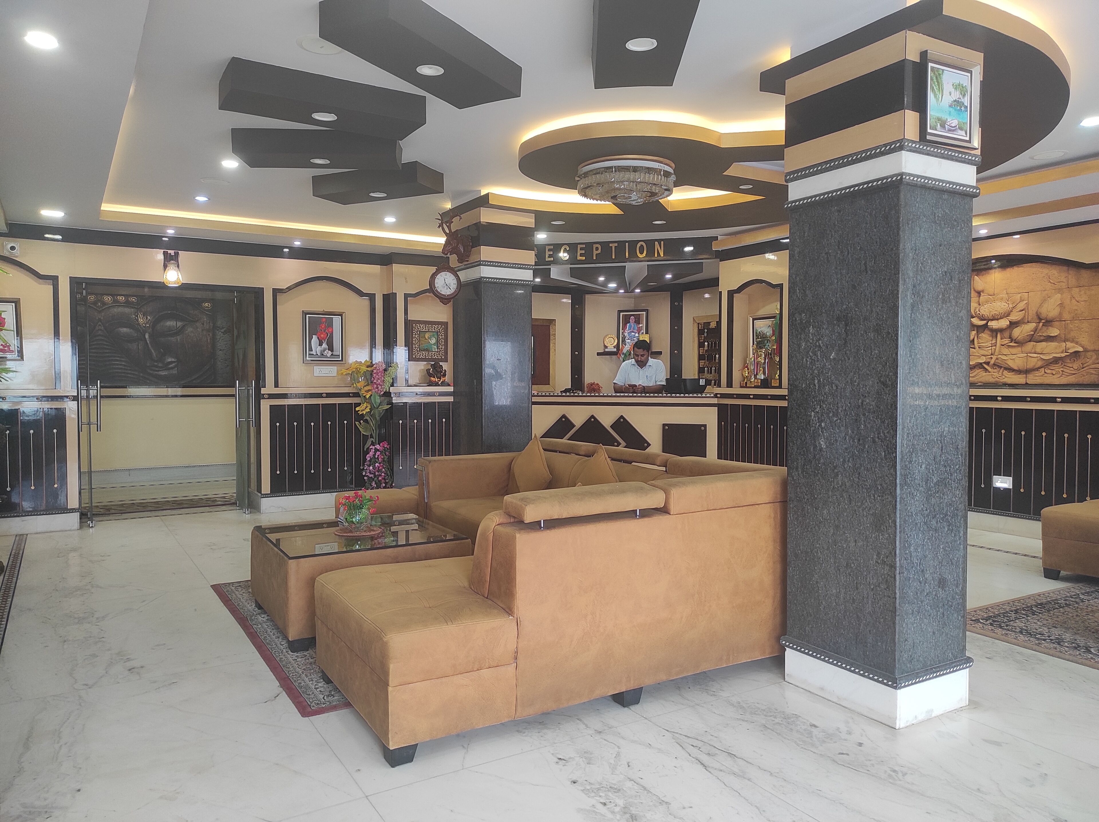 A lobby with a reception desk, a sofa, a pillar, and a chandelier.