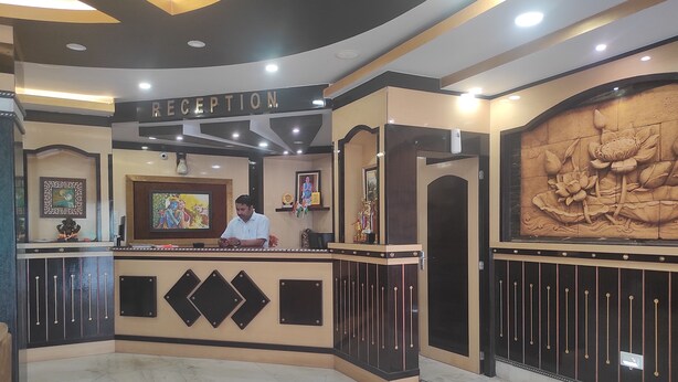 A reception area with a sign reading "RECEPTION," a man at the counter, and a decorative wall with floral carvings.