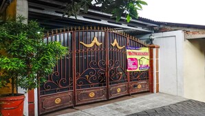 A gated entrance with a decorative iron gate, a potted plant, and a sign advertising a house tour. - OYO 90846 Guesthouse Bintaro Asri Syariah (South Tangerang)